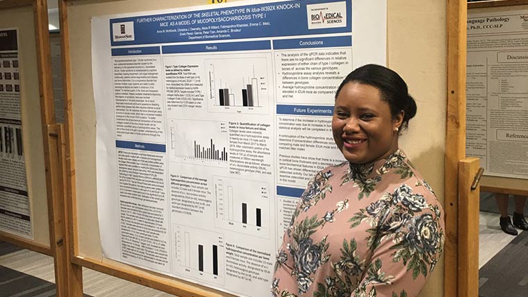 Biomedical sciences student standing next to their research poster at a research symposium.