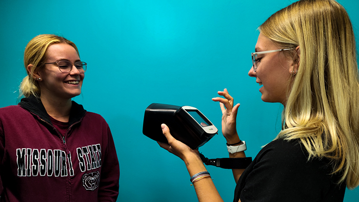 An AmeriCorps member tests a Missouri State student's eyes using the digital vision screener camera