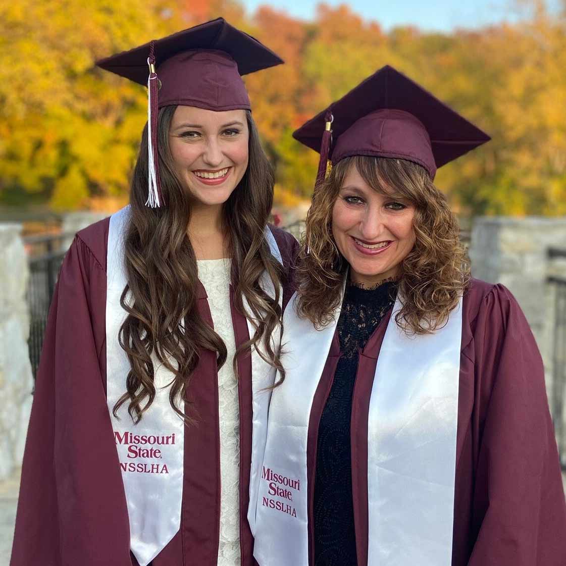 Hannah and Julie Anderson wearing maroon commencement mortarboards and gowns during their graduation