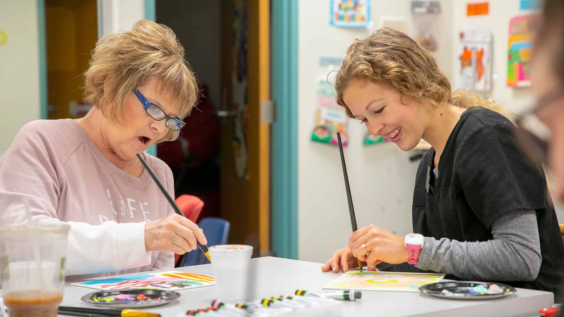 A speech-language student paints with an adult patient during a group therapy session