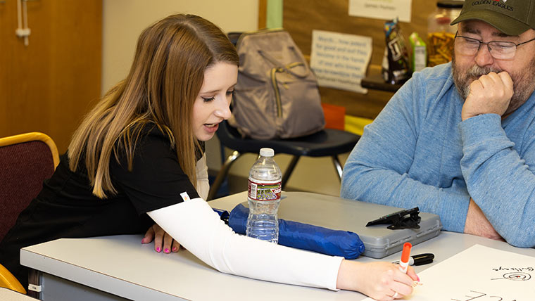 A speech-language pathology student writes on a poster board during an adult group therapy session.