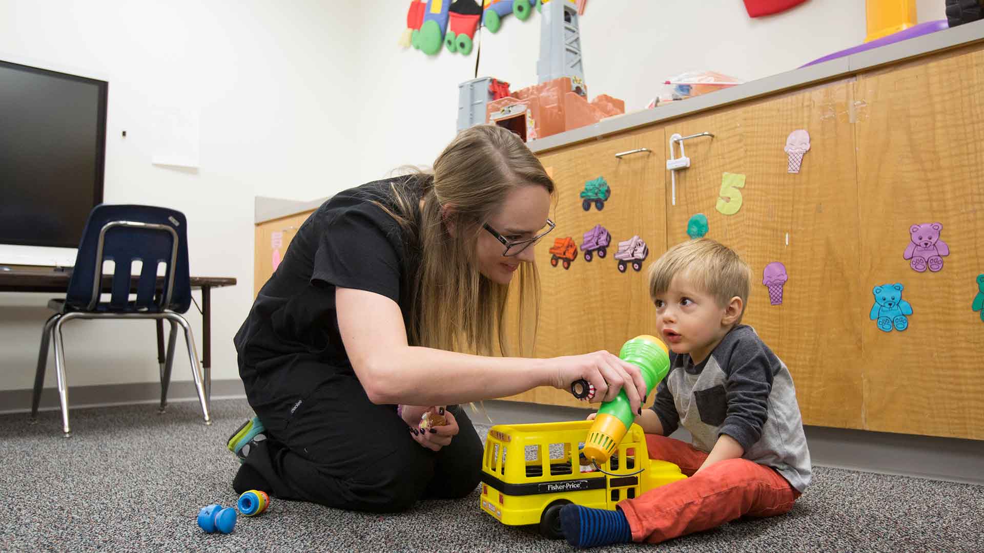 A speech-language student does a therapy session with a young child in a play area.