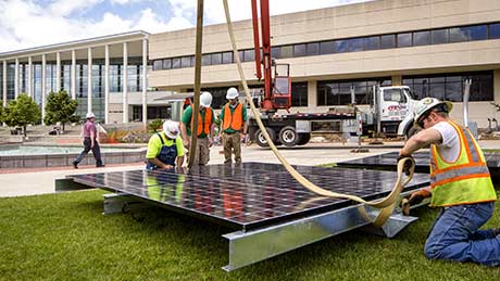 Workers preparing to hoist a solar panel in place in front of Meyer Library
