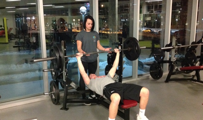 Guy bench pressing while being spotted by gym partner.