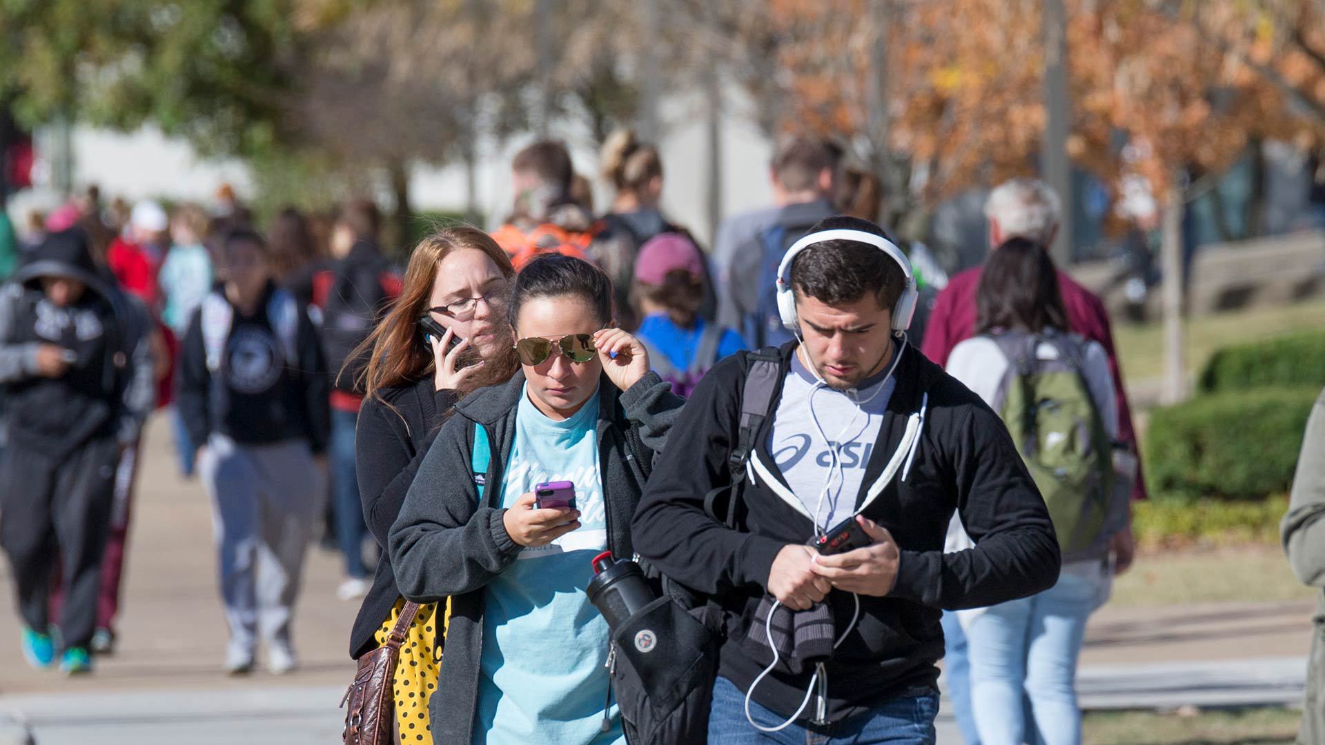 Students walking across campus using their smartphones
