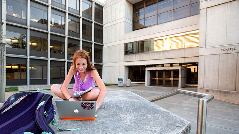 Missouri State student viewing laptop outside on campus