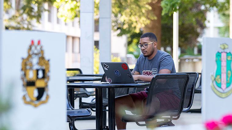 Transfer student at laptop outside on campus