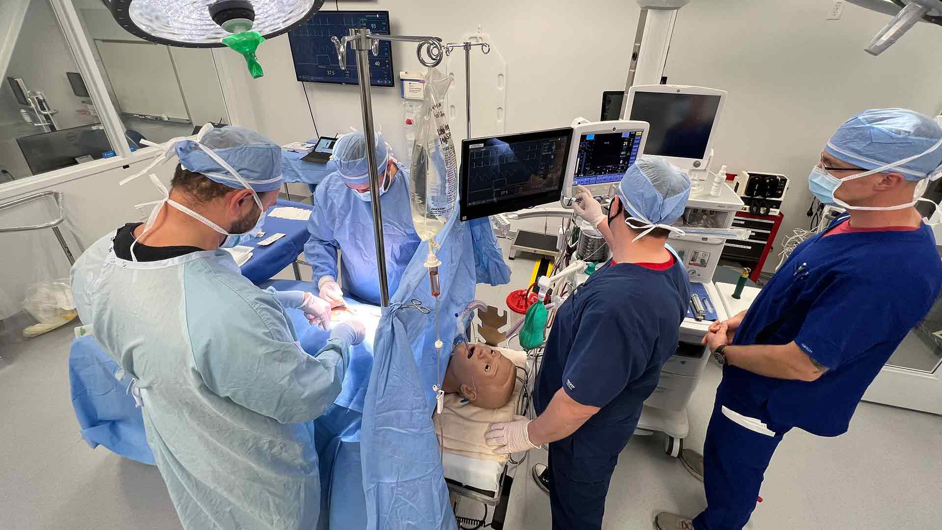 Surgeons and nurse anesthetists practicing on a mannequin in a surgery room.