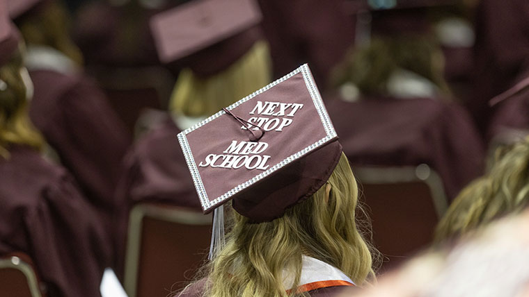 Student at graduation with her cap saying, 'next stop, med school.';
