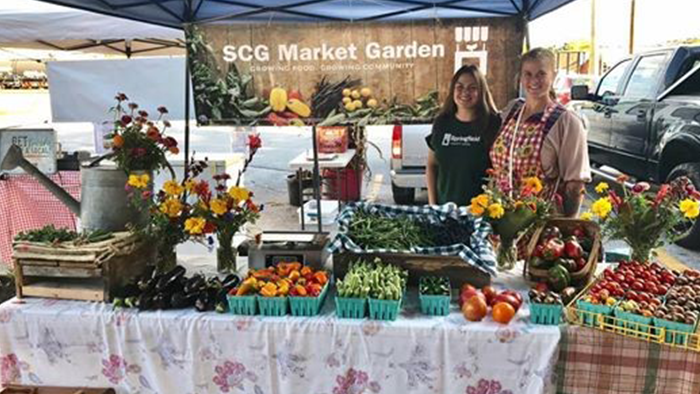 Two young women smile at the camera behind a SCG Market Garden booth