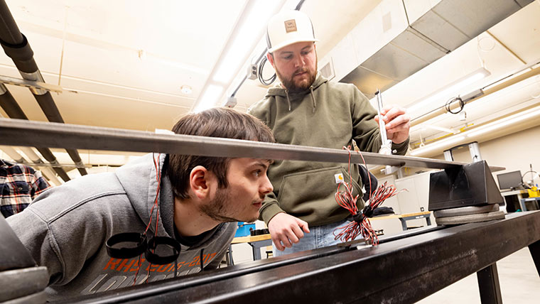 Two civil engineering students testing a metal beam during a lab class.