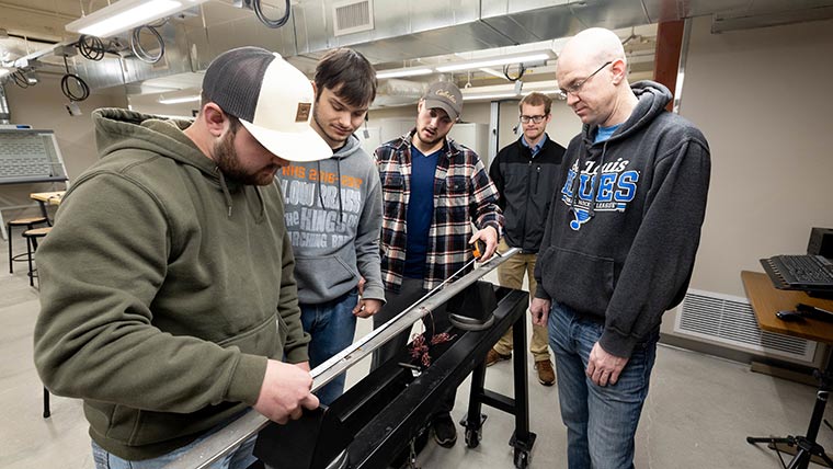 A group of students taking measurements on a four-foot long aluminum beam.