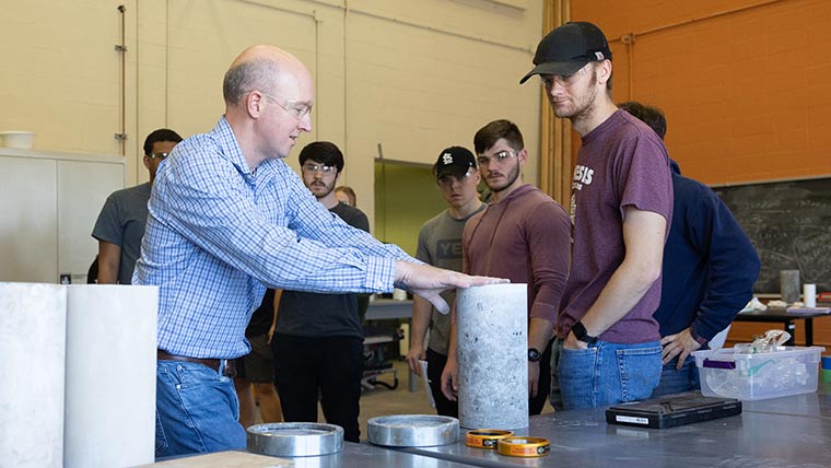 Dr. Matt Pierson handling a concrete block while a group of students watch.
