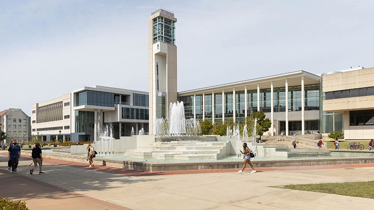 Students walking by the campus fountain with Meyer Library and Glass Hall in the background.