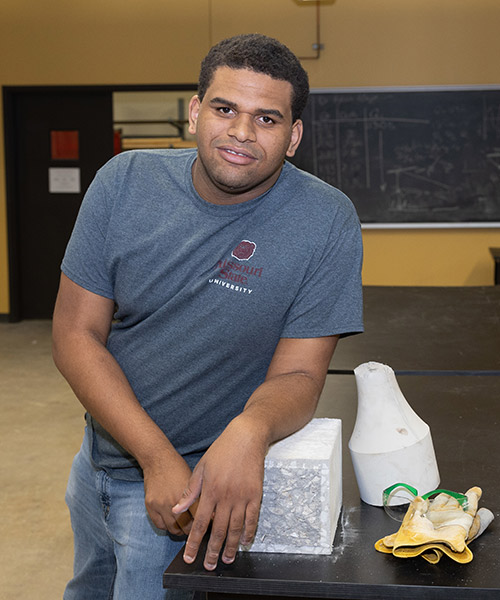 Luther Harris posing for a photo in an engineering lab at Missouri State. His left arm is resting on a concrete block.