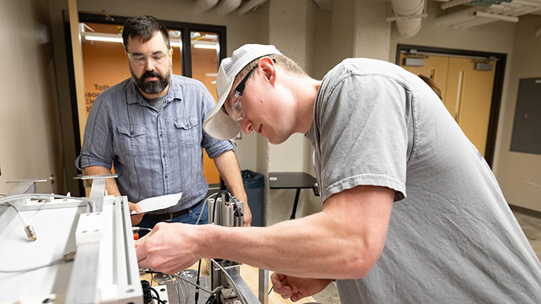 A mechanical engineering student preparing to use equipment during a lab class. His professor is watching to make sure it's properly done.