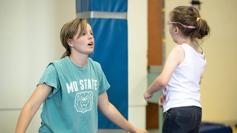 Student helping young girl in exercise class.