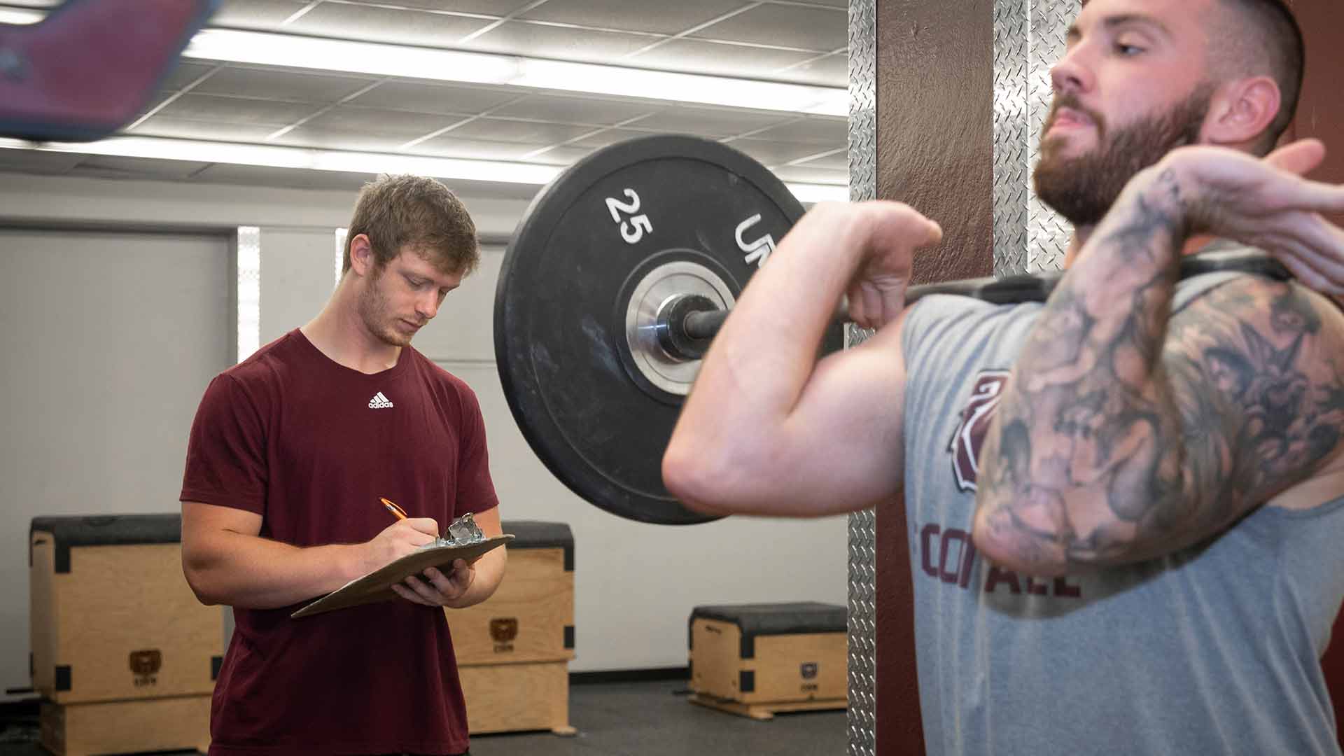 Strength coach supervising football player lifting weights