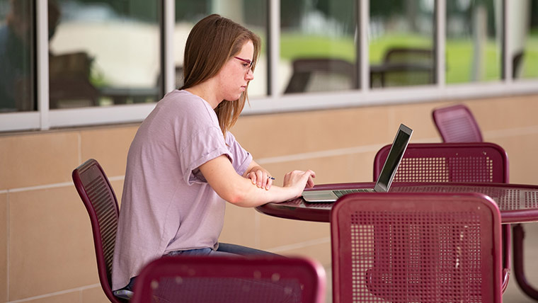 Student sitting outside using laptop.