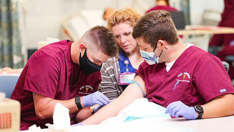 Teacher assisting a student putting an IV into another student.