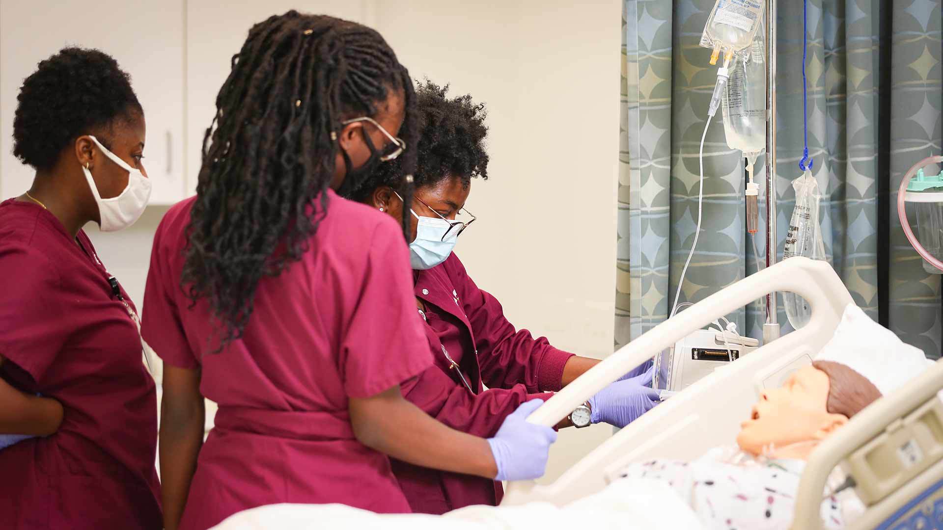 Three nursing students working on a fake patient in a skills lab.
