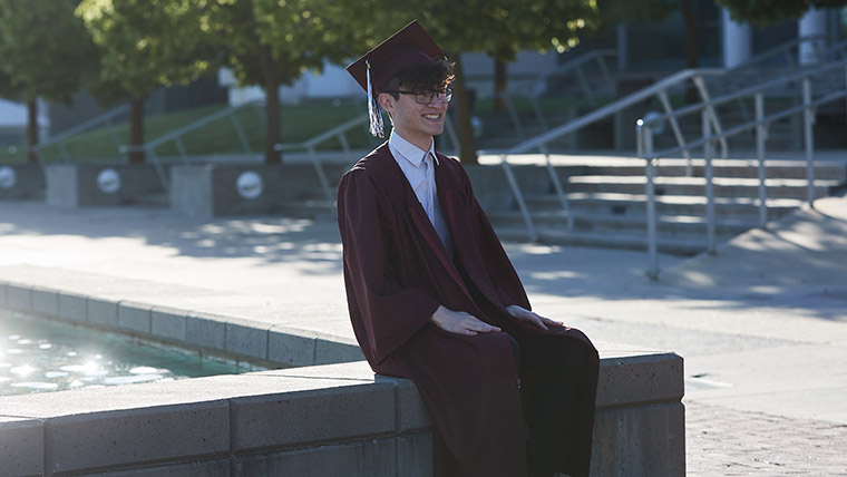 Missouri State graduate in cap and gown sitting by fountain.
