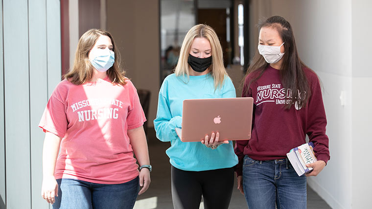 Nursing students walking down hallway while looking at laptop.