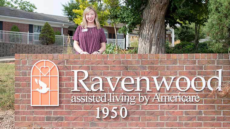 Student standing by Ravenwood Assisted Living sign.