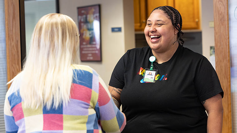 A social worker laughing and talking with a co-worker in an office setting.