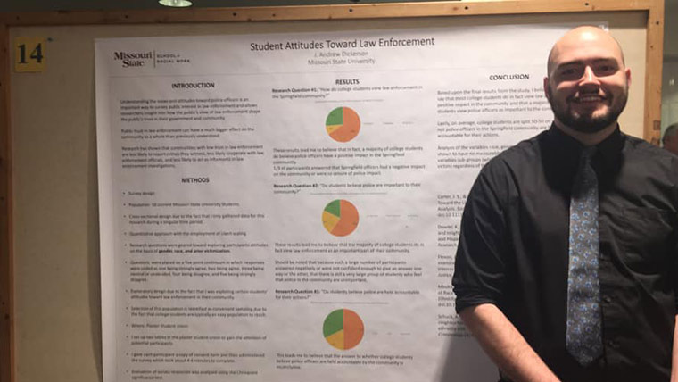 A social work student posing next to his research poster at a symposium.