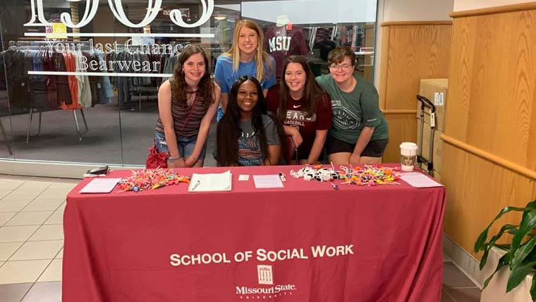 Members of the Social Work Club posing for a photo behind a table during Welcome Weekend.
