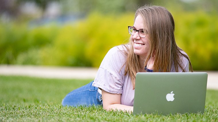Missouri State student lying on the grass with her laptop. 