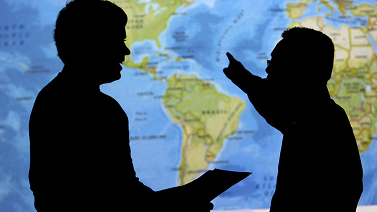 Silhouette of two people talking in front of a global map.
