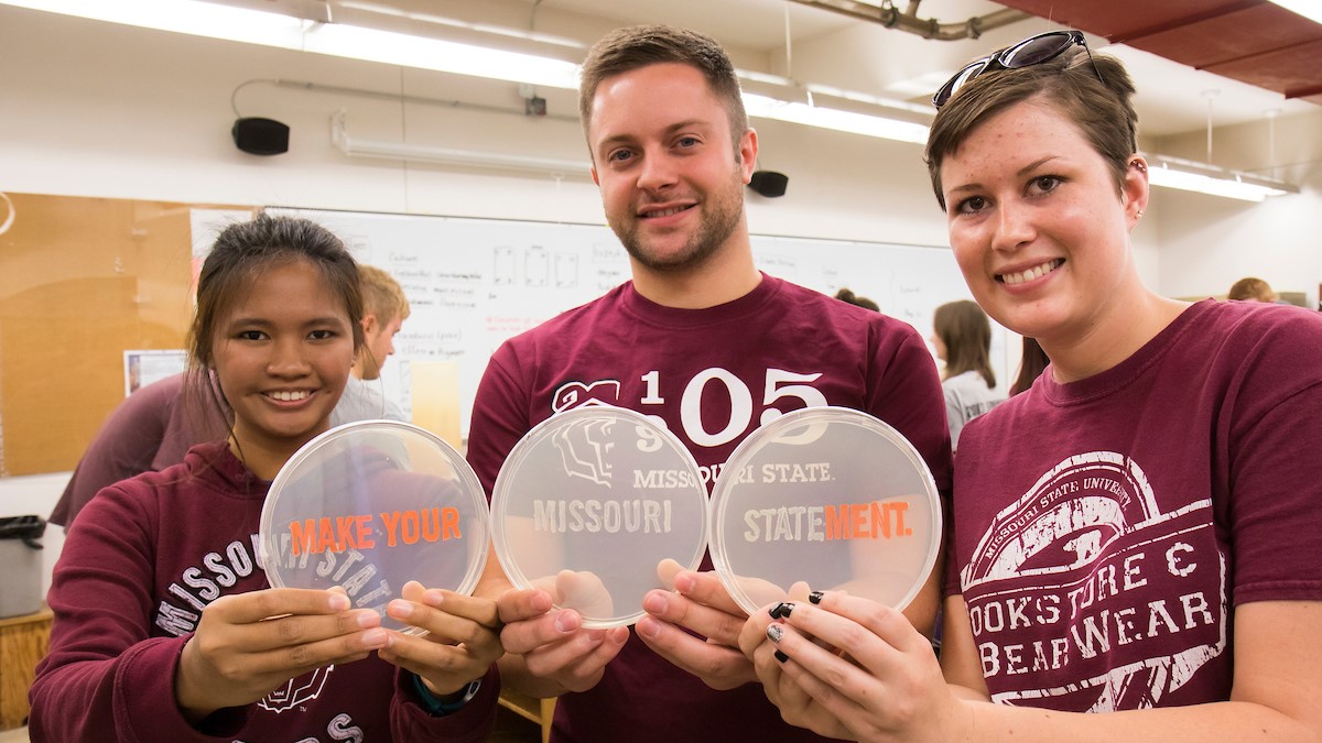 Three Missouri State students proudly display a bacteria growth science project that reads 'Make Your Missouri Statement.'