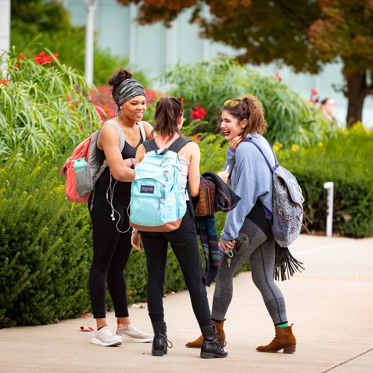 Three students talk on sidewalk in spring