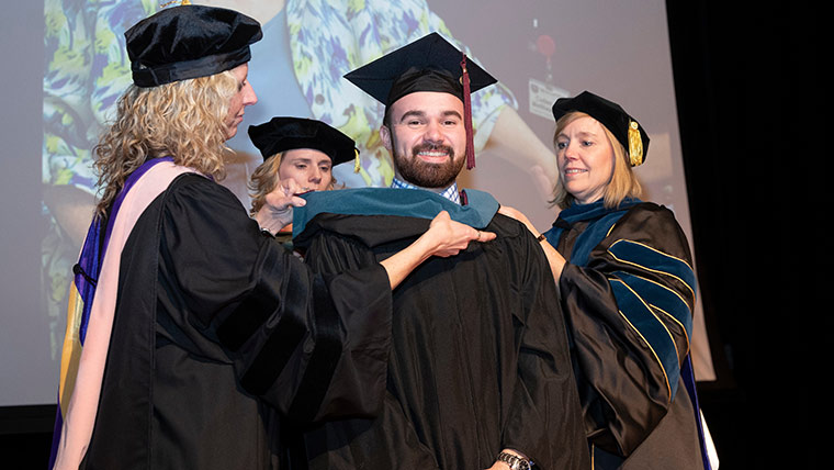 Occupational therapy student receiving slate blue hood from faculty at graduation ceremony