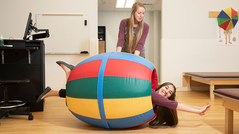 OT student hanging out from an inflatable tube as another OT student pushes her around.