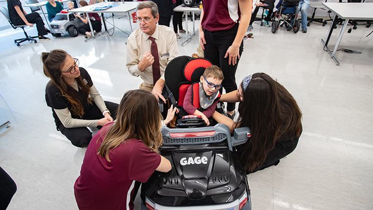 Students and faculty member helping a child with developmental disabilities fit into a mobility vehicle.