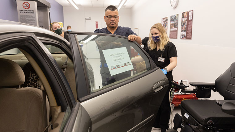 Occupational therapy students help a client get into a car.