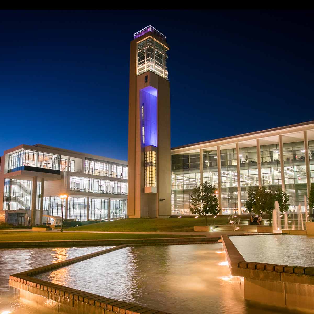 A gorgeous nighttime view of Meyer Library, the Carillon and Glass Hall with their lights on and the campus fountain running in the forefront.