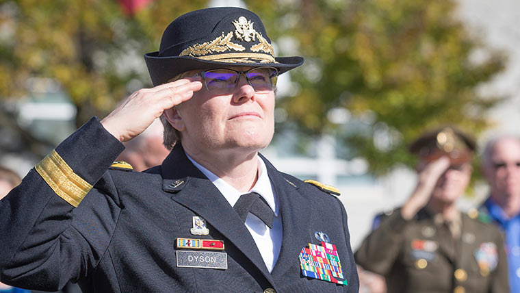 Karen Dyson in uniform and saluting the flag during a Veteran's Day event on campus.