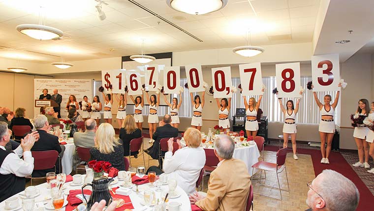 A banquet event celebrating a fundraising campaign by the Missouri State Foundation. Cheerleaders are holding up numbers that display the total amount raised: $167,000,783 million.