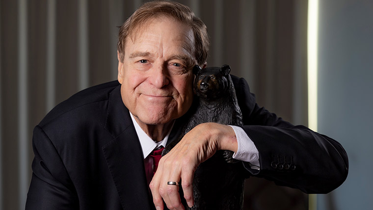 Actor John Goodman posing with a small Bear statue.