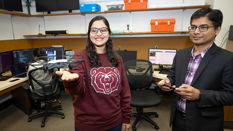 A computer science student holds a drone for takeoff as her professor works the controller.