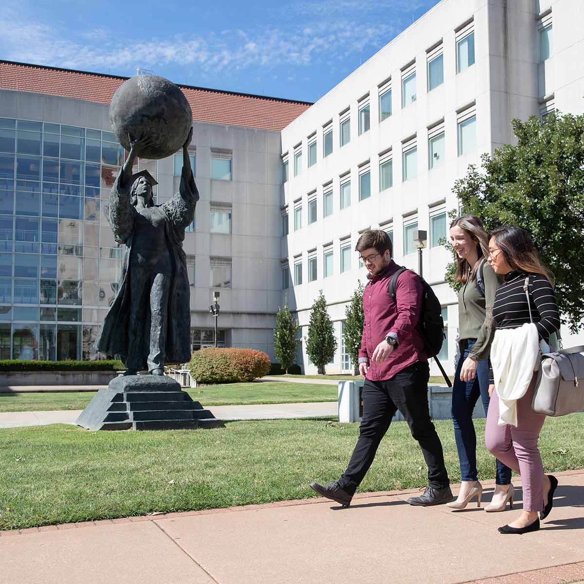 Three graduate students walking by the Citizen Scholar statue in front of Strong Hall.