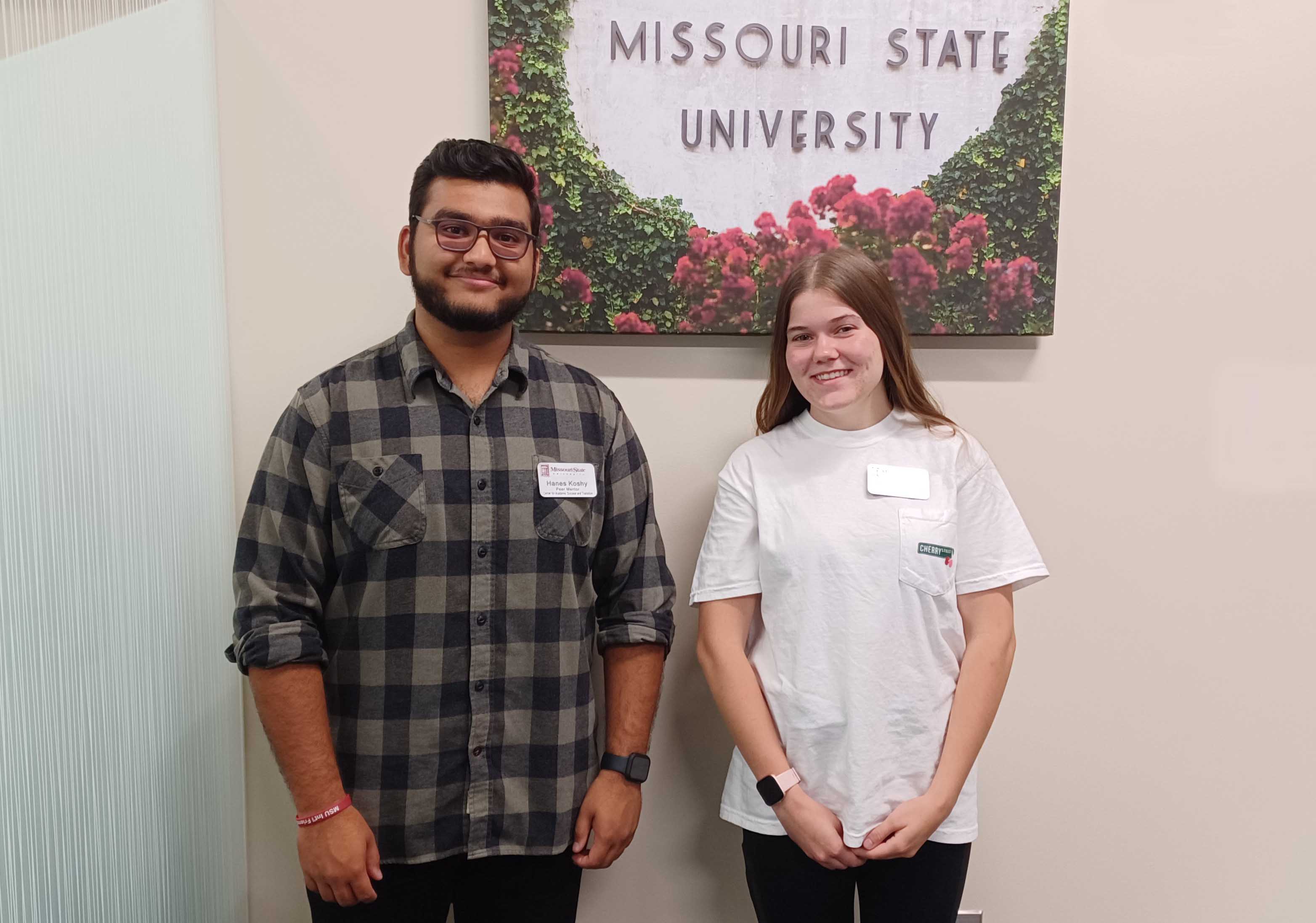Two peer mentors stand in front of a canvas print with the words Missouri State University.