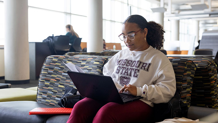 A student viewing her laptop in a library looking at the next steps of an admitted student