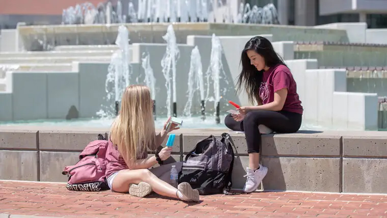 Two Missouri State students sitting and eating popsicles by Hammons fountains. 