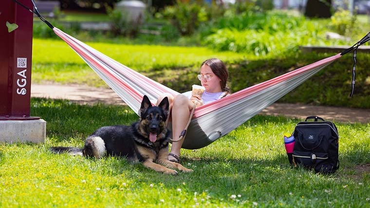 Missouri State student sitting in a hammock on campus with her dog at her feet.