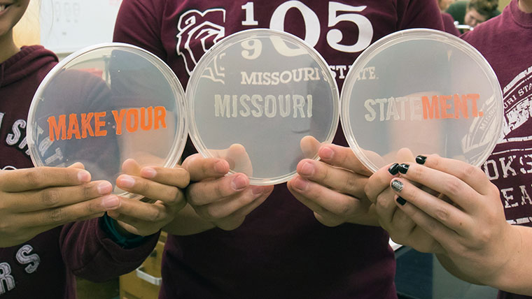 Three Missouri State students holding Petri dishes that say MAKE YOUR MISSOURI STATEMENT